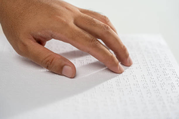 hand of a blind person reading some braille text on page paper to learn. finger of blind student touching the braille alphabet code on sheet. - blindenschrift stock-fotos und bilder