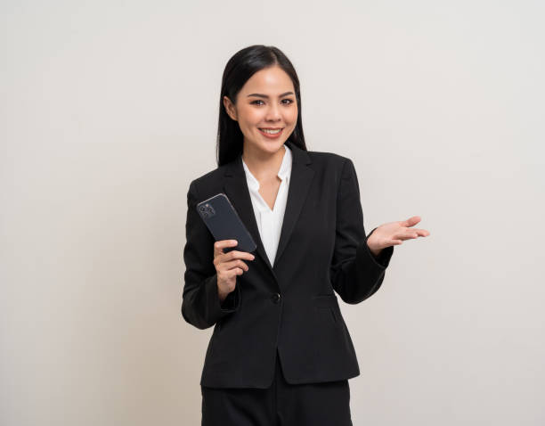 Attractive elegant young asian business woman using cellphone standing on isolated background. Happy Excited young asian female formal black suit holding smartphone contract service with customer