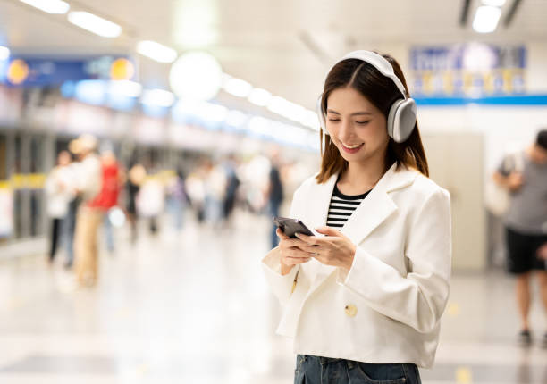 istock Young asian woman using smartphone application navigate location destination while travel by subway. Asian female with headphone listen to the music by cell phone while traveling in train transport 2155812348
