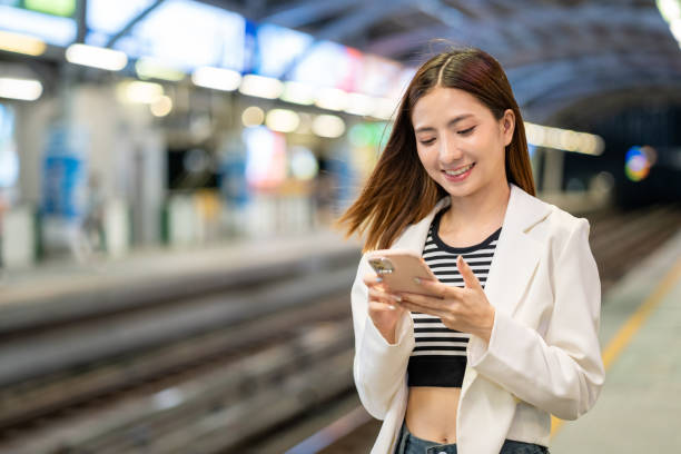 istock Young asian woman using smartphone application navigate location destination while travel by train. Asian female with cell phone standing near railway platform in train station. 2155812404