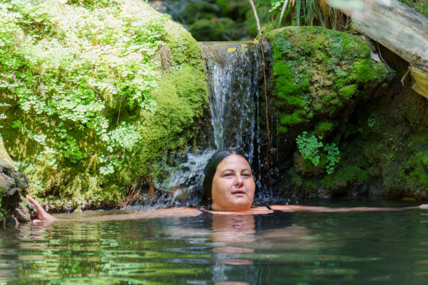 Rear-view photo of a young Hawaiian woman wading in a pool near a remote Hawaiian waterfall with arms outstretched skyward in joy