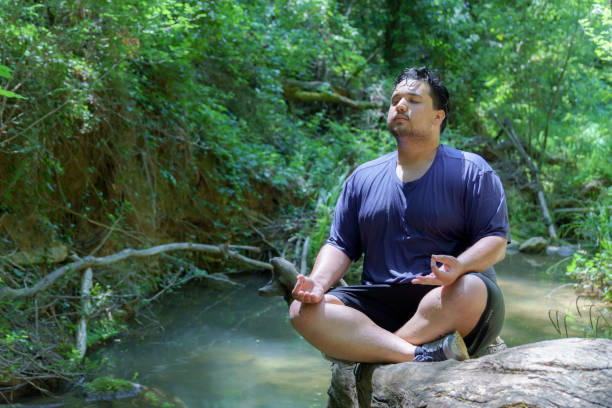 istock young boy in a blue T-shirt meditating sitting on a tree trunk over a river 2155814478