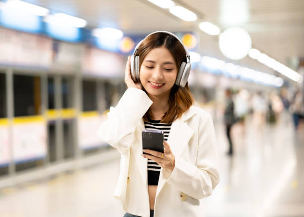 istock Young asian woman using smartphone application navigate location destination while travel by subway. Asian female with headphone listen to the music by cell phone while traveling in train transport 2155814691