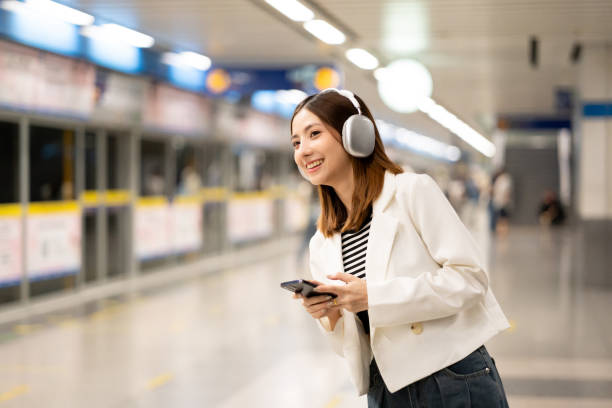 istock Young asian woman using smartphone application navigate location destination while travel by subway. Asian female with headphone listen to the music by cell phone while traveling in train transport 2155816079