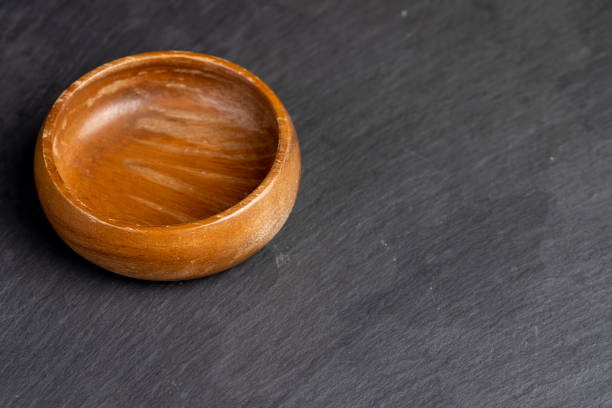 an empty wooden bowl on a black stone board, an old wooden round bowl on a black surface
