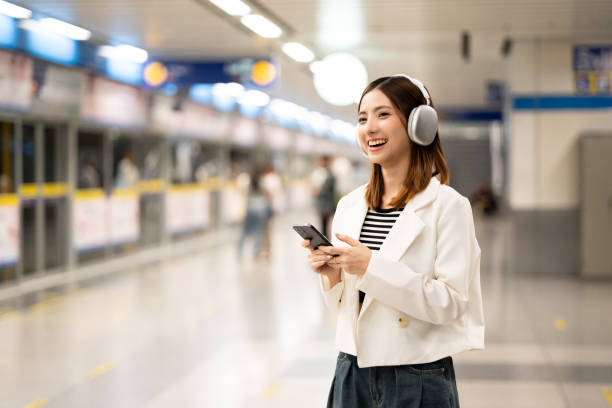 istock Young asian woman using smartphone application navigate location destination while travel by subway. Asian female with headphone listen to the music by cell phone while traveling in train transport 2155820532