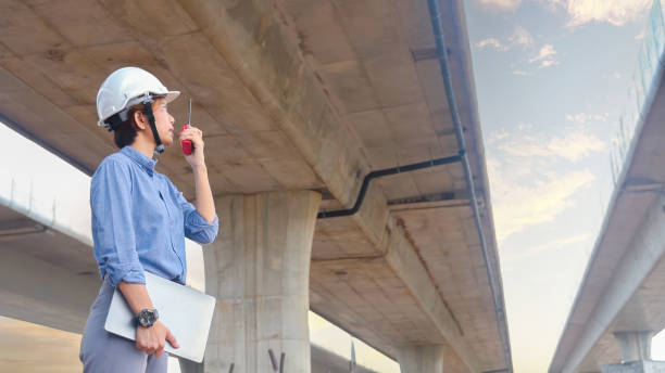 Asian female engineer using walkie talkie at construction site Standing near the concrete road, highway bridge.