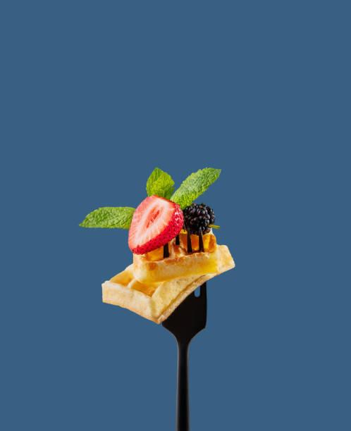 istock Wafer pieces with fresh strawberries, blackberries, mint leaves  on a black fork on a blue background. Sweet dessert concept with fruits. 2155827082