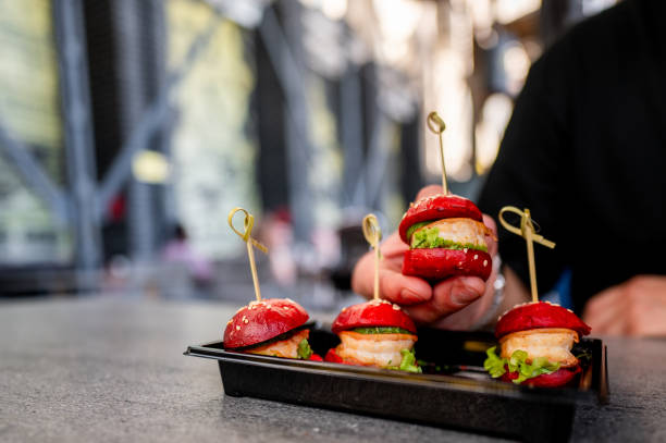istock A hand holds a mini burger with three others on a tray, creatively garnished with colorful spices. 2155831932
