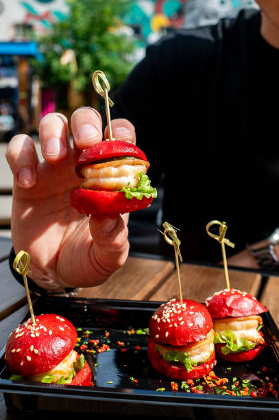 istock A hand holds a mini burger with three others on a tray, creatively garnished with colorful spices. 2155831933