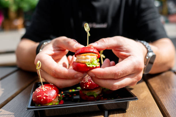 istock A hand holds a mini burger with three others on a tray, creatively garnished with colorful spices. 2155831934