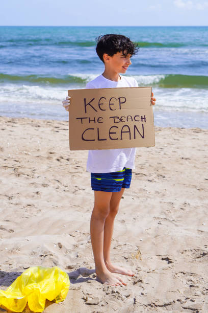 istock boy picking up plastic on the beach and holding up a sign saying KEEP THE BEACH CLEAN 2155834699