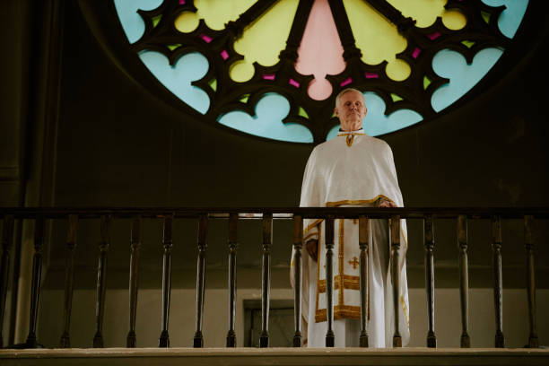 Wide shot of senior Caucasian Catholic priest wearing liturgical vestment standing at mezzanine in church, copy space