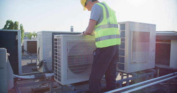 istock Maintenance worker or engineer wearing protective helmet and visibility yellow vest examining AC unit fan outdoors and taking notes 2155840367