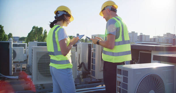istock Maintenance workers or engineers wearing protective helmets and yellow vests inspecting AC unit fan outdoors on a roof comparing notes 2155840375
