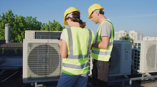 istock Maintenance workers or engineers wearing protective helmets and visibility yellow vests examining a new AC unit fan on the roof outdoors and taking notes 2155840379