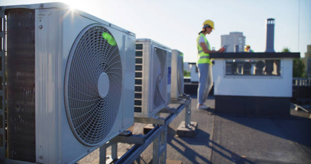 istock Maintenance worker or engineer wearing protective helmet and visibility vest examining AC unit fan outdoors and taking notes 2155840416