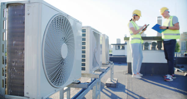 istock Maintenance workers or engineers wearing protective helmets and yellow vests examining a new AC unit fan outdoors together and taking notes 2155840422