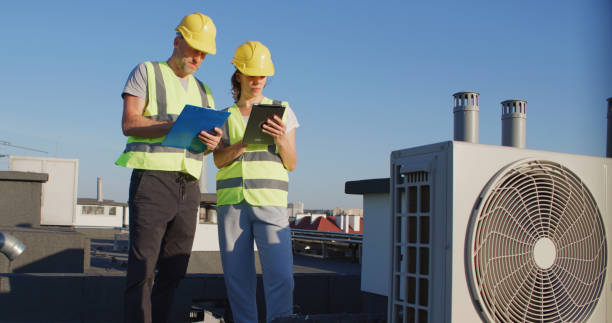 istock Maintenance workers or engineers wearing protective helmets and visibility yellow vests examining AC unit fan together 2155840427