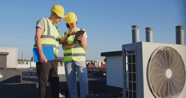 istock Maintenance workers or engineers wearing protective helmets and visibility yellow vests examining AC unit fan outdoors together 2155840430
