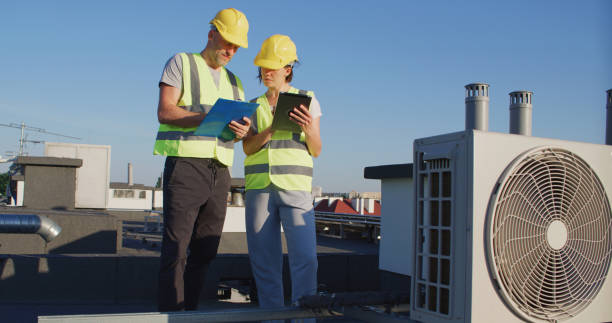 istock Maintenance workers or engineers wearing protective helmets and visibility yellow vests examining AC unit fan outdoors 2155840433
