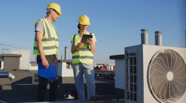 istock Maintenance workers or engineers wearing protective helmets and visibility vests examining AC unit fan outdoors together 2155840438