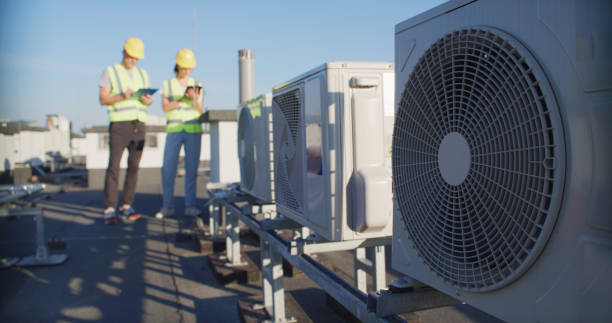 istock Maintenance workers or engineers wearing protective helmets and visibility yellow vests examining AC unit fan outdoors together and taking notes 2155840439