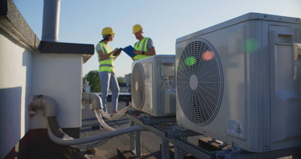 istock Maintenance workers or engineers wearing protective helmets and visibility vests examining AC unit fan outdoors together and taking notes 2155840443