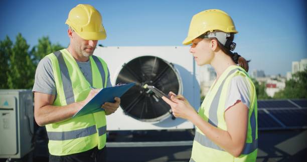 istock Maintenance workers or engineers wearing protective helmets and visibility inspecting AC unit fan outdoors on a roof comparing notes 2155840469