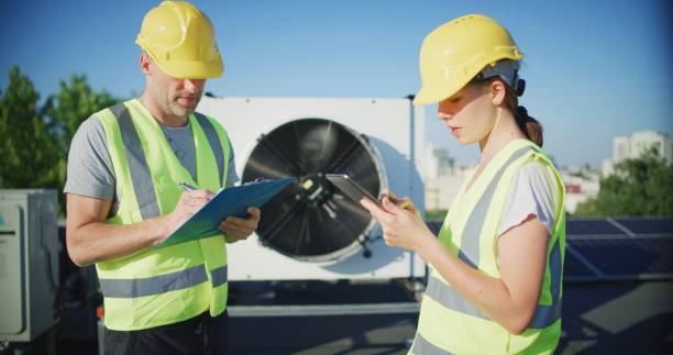 istock Maintenance workers or engineers wearing protective helmets and yellow vests inspecting AC unit fan outdoors on a roof 2155840471