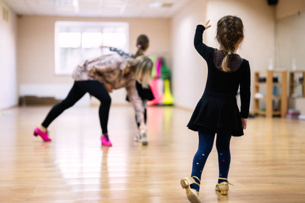 A young girl in a dance class practicing with guidance from an instructor. She is wearing a black outfit and following dance steps.