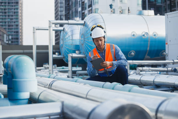 istock Man engineer holding tablet working at rooftop building construction. Male technician worker working checking hvac of office building. Engineering installing large air conditioning system. 2155848653
