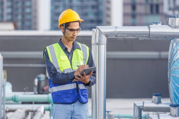 istock Man engineer holding tablet working at rooftop building construction. Male technician worker working checking hvac of office building. Engineering installing large air conditioning system. 2155848746
