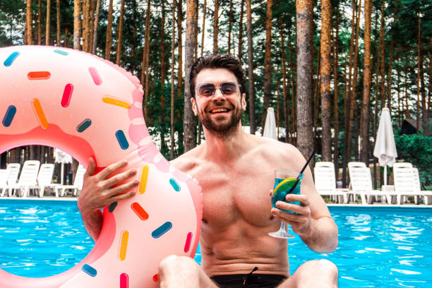 istock Happy young man holding inflatable ring and cocktail while resting in the swimming pool outdoors. Summertime, holidays, lifestyle concept 2155853685