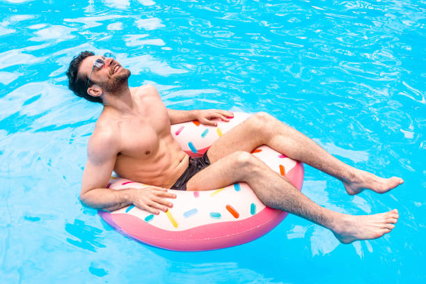 istock Smiling guy in sunglasses enjoying his vacation while swimming with inflatable ring in the pool outdoors. Summertime, holidays, lifestyle concept 2155853705