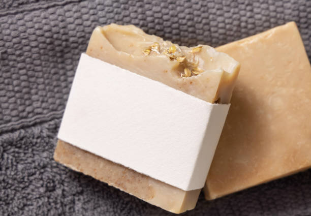 istock Beige handmade soap bar with blank label on dark grey folded towel top view, mockup 2155860127