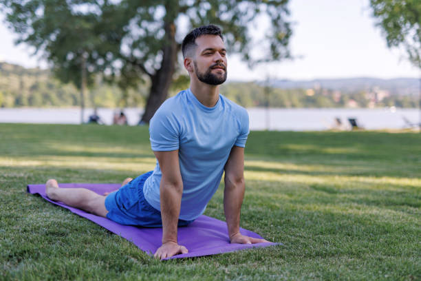Demonstrating strength and flexibility, a man executes the upward dog yoga pose on a mat in a park, reflecting his commitment to sports training and a muscular build as part of a healthy lifestyle