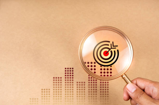 Business target growth concept. Bullseye dartboard icon on business graph expanded in magnifying glass lens in hand for focus business goal trends, brown background with copy space, minimal and eco.