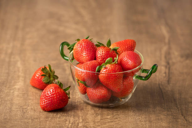 Fresh strawberries in a glass bowl on wooden table .