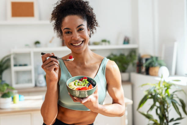 istock Athletic woman eating a healthy fruit bowl while looking at camera in the kitchen at home 2155873749