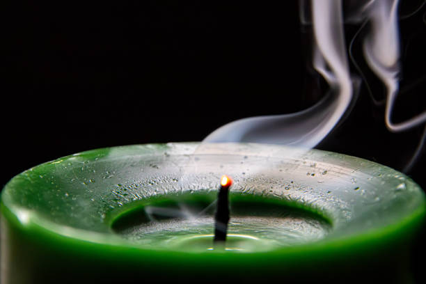 A green scented candle emitting steam in darkness.