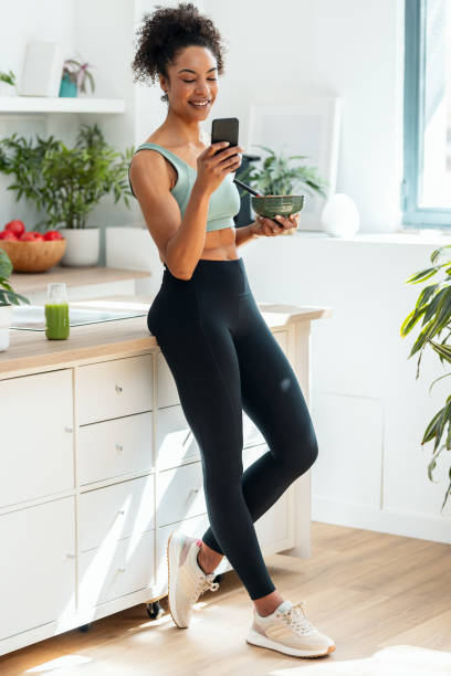 istock Athletic woman eating a healthy fruit bowl  while using smartphone in the kitchen at home 2155874895