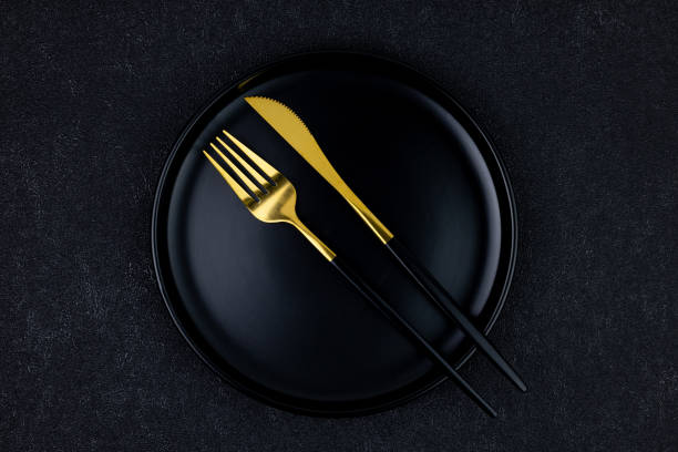 istock Black plate with fork and knife on black concrete background, top view 2155877675