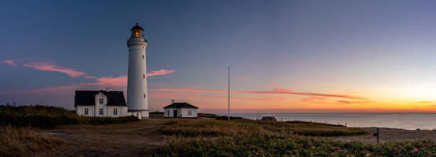 Hirsthals, Denmark – August 10, 2022: A lighthouse illuminated at sunset on a beach at night