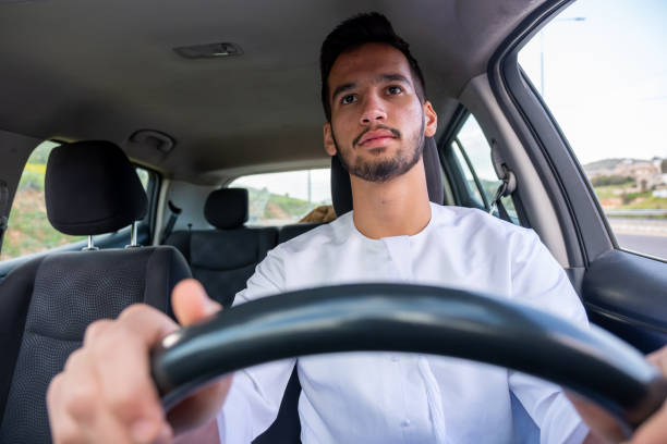 istock A cheerful young man with a beard, wearing a traditional Middle-Eastern outfit, smiles confidently while seated in his car. He appears to be enjoying a drive through a scenic countryside 2155883064