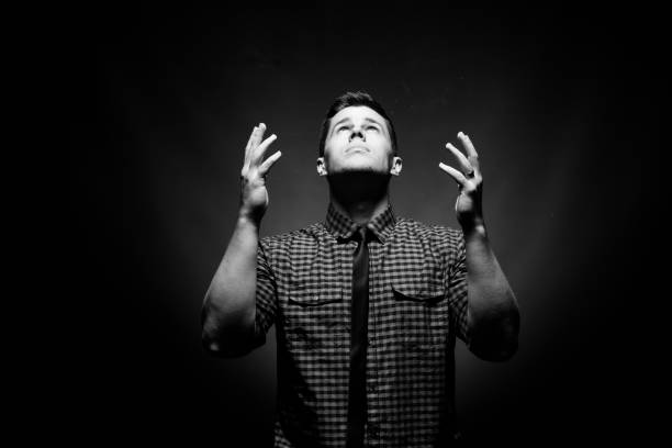 A black and white photo of a man looking up with open hands in surrender.