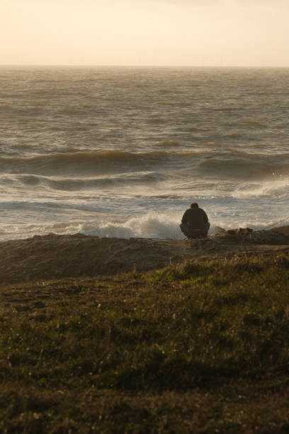 A man sitting on the shore, watching waves at sunset