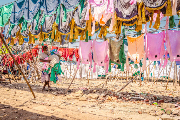 Mumbai, India – April 15, 2015: A man carrying laundry under vibrant hanging clothes in Mumbai sunlight, India