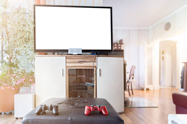 A widescreen TV with Copy Space. In the foreground are joysticks and a game console. Authentic home interior.