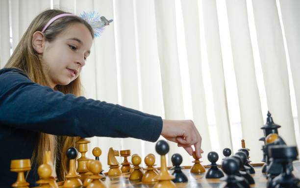 istock a girl with a crown looking at her chess game piece 2155896397